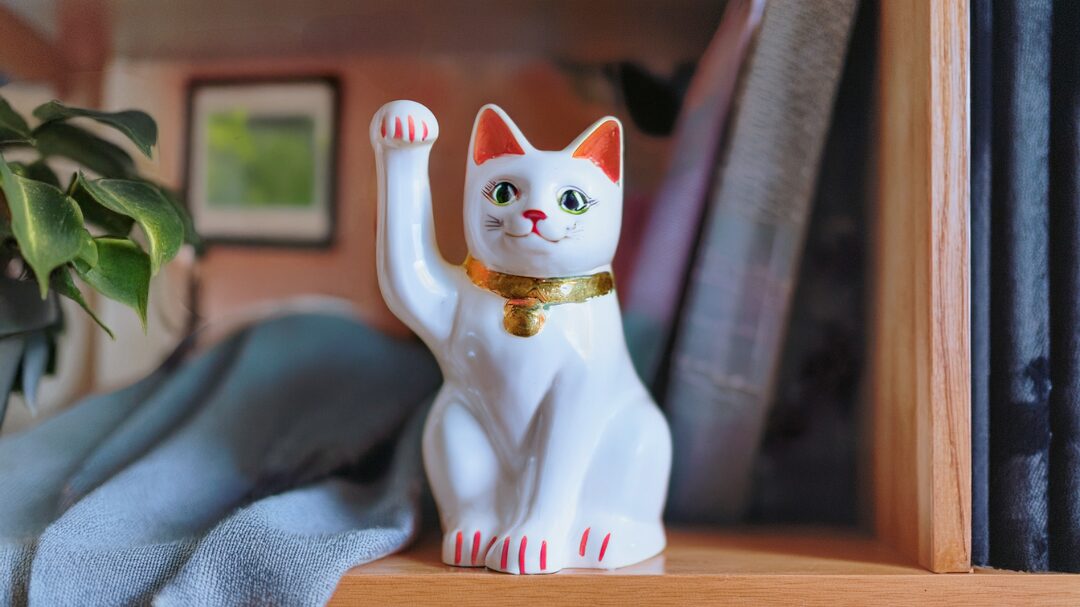 棚の上に置かれた白い招き猫の置物。片手を上げて微笑む姿が、風水で幸運を招く象徴として表現されている。
